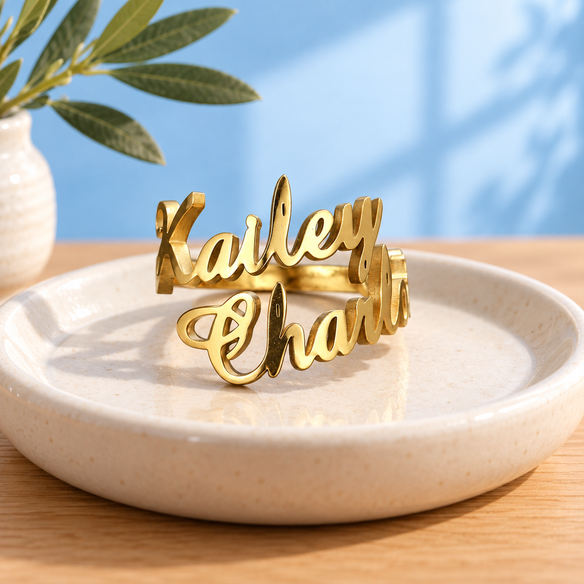 Personalised two-name stainless steel ring in Gold on an ivory dish against the Cary & Co blue background