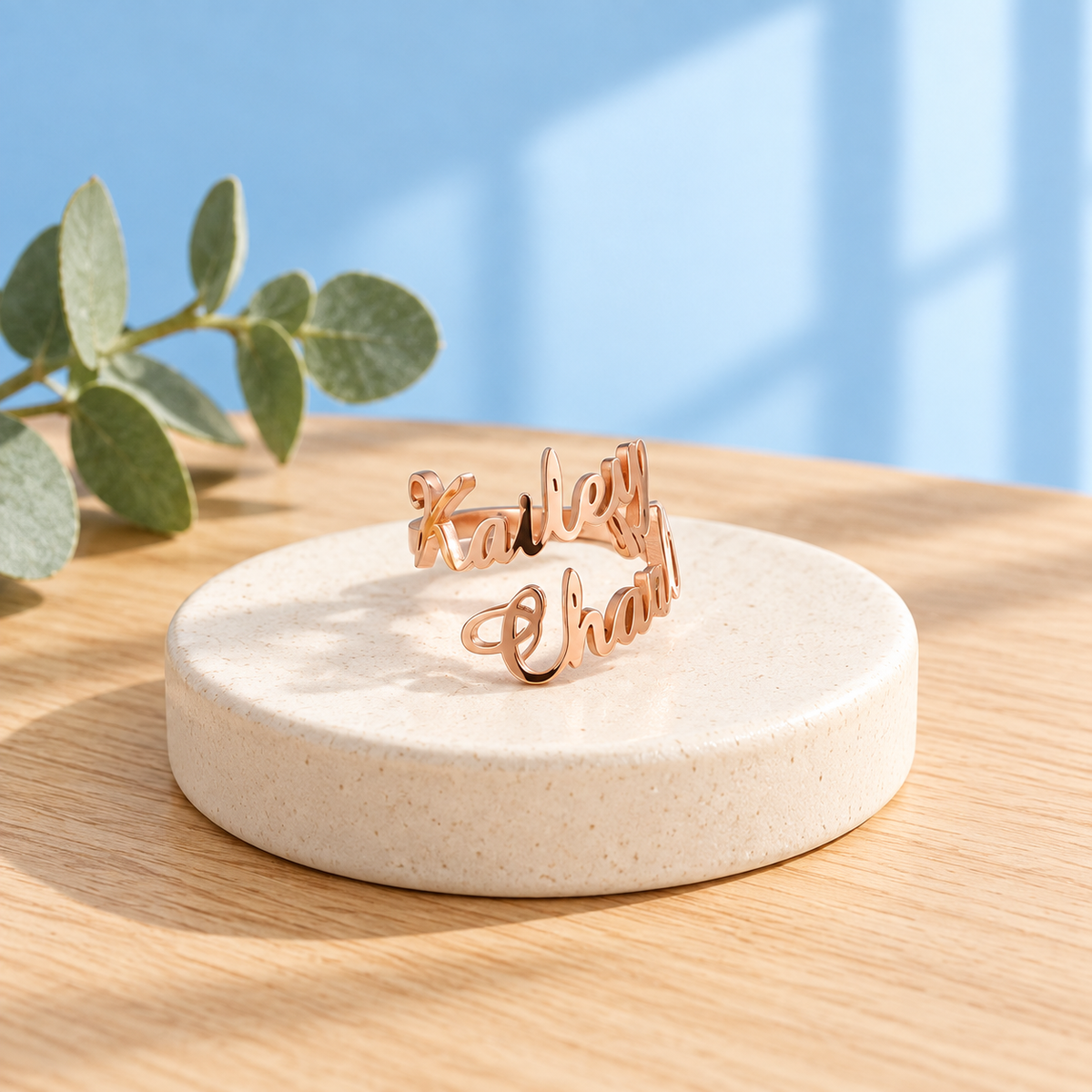 Personalised two-name stainless steel ring in Rose Gold on an ivory pedestal against the Cary & Co blue background
