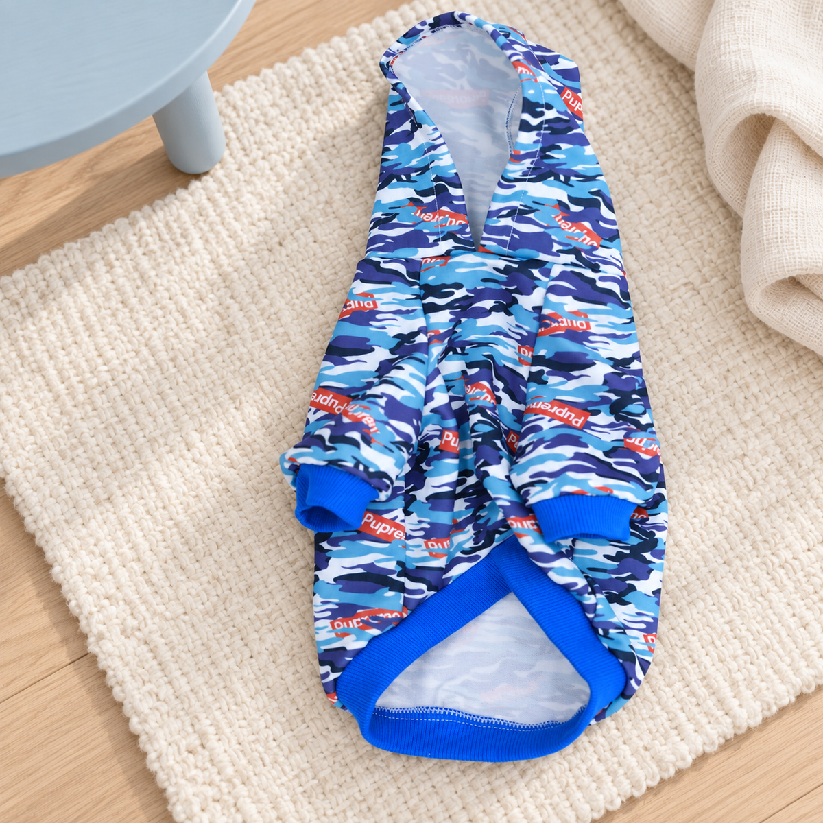 Blue camouflage dog hoodie on an ivory rug, showing the front opening and hood lining